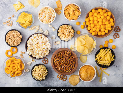 Alle klassischen Kartoffel Snacks mit Erdnüssen, Popcorn und Zwiebelringen und gesalzene Brezeln in Schüssel Platten auf Leuchtkasten. Twirls mit Stöcken und Kartoffelchips Stockfoto