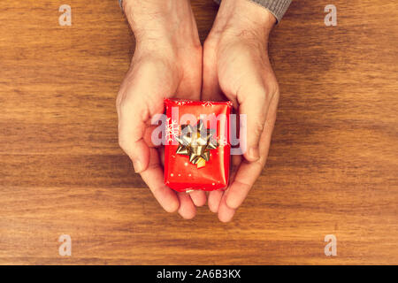 Ein Mann hält ein Weihnachtsgeschenk an einem hölzernen Tisch Stockfoto