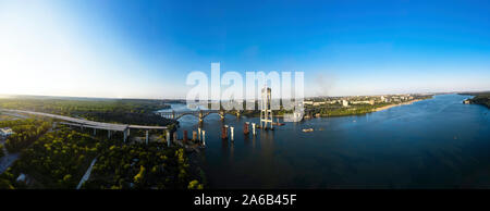 Antenne Panorama der Unvollständige Automobil Brücke und Arch Bridge im Hintergrund des Wasserkraftwerks. Industrielle Stadt. Stockfoto