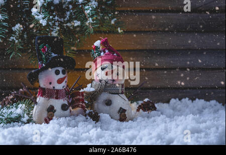 Nacht Szene von zwei Urlaub Schneemänner Figuren mit fallenden Schnee auf einem rustikalen Holzmöbeln Hintergrund mit Kopie Raum Stockfoto