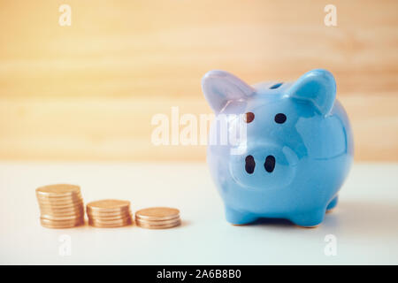Piggy Bank mit drei Stapel von Münzen auf einem weißen und Holz- Hintergrund. Flare. Stockfoto