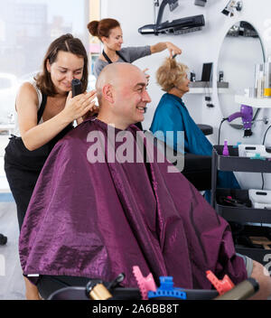 Professionelle friseur Frau tun Styling der glatzköpfige Mann mit elektrischen Trimmer bei Friseur Stockfoto