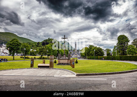 LOURDES - JUNI - 15 - 2019: christliche Kreuz auf einem Hintergrund der Basilika Unserer Lieben Frau vom Rosenkranz in Lourdes, Frankreich Stockfoto