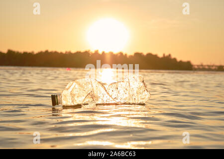 Zerknitterte transparenten Kunststoff Flasche schwimmt auf der Oberfläche des Wassers. Sonnenuntergang, grünen Bäumen. Die Menschen und der Ökologie. Riverside Umweltverschmutzung. Erhaltung der Stockfoto