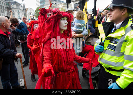 London, 10. Oktober 2019, vom Aussterben Rebellion Gruppe in rot Kostüme surround Polizei acivists vorbereiten, die sich um eine Holz- struktur in der Straße neben dem Trafalgar Square gesperrt haben zu verhaften. Stockfoto
