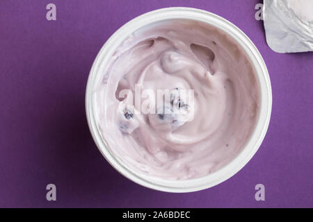 Heidelbeere Joghurt in Schale aus Kunststoff mit Deckel Folie auf der Seite und auf Deep Purple Hintergrund isoliert - Ansicht von oben Stockfoto