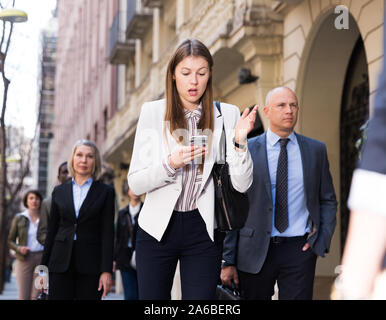 Junge besorgt business Frau an ihrem Smartphone suchen Bei einem Spaziergang in überfüllten Stadt Straße Büro Stockfoto