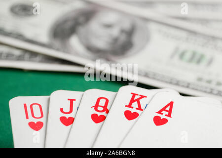 Nahaufnahme der Kombination von Royal Flush der Herzen Karten beim Poker auf dem Hintergrund der dollarscheine am grünen Tisch. Stockfoto