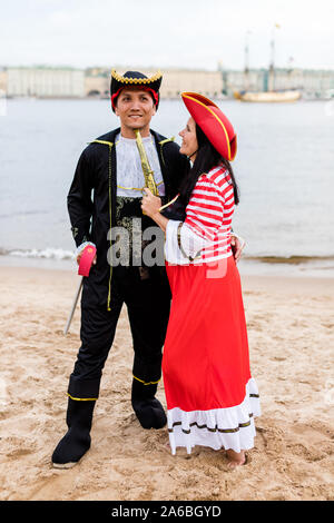 Junge glücklich kaukasische Frau in Piraten Kostüm eine Pistole an den lächelnden Mann auf Sandstrand. Vertikale. Stockfoto