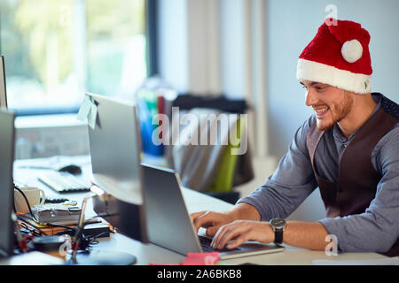 Junge lächelnde Geschäftsmann an einem Computer an Weihnachten arbeiten Stockfoto
