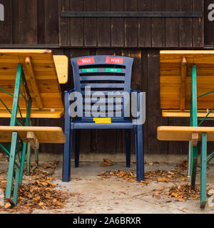 Ein leerer Stuhl mit dem Wort "Wirt" in deutscher Sprache steht zwischen Tabellen außerhalb einer geschlossenen Cafe geschrieben Stockfoto