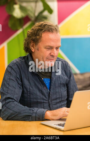 Ein Mann sitzt an einem Schreibtisch im Zimmer, der an einem Notebook arbeitet Stockfoto