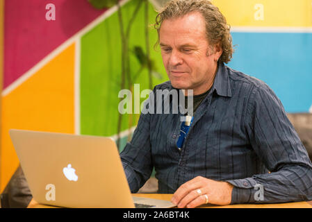 Ein Mann sitzt an einem Schreibtisch im Zimmer, der an einem Notebook arbeitet Stockfoto