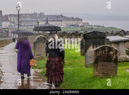 Zwei Frauen in traditionellen Goth Kostüme im Regen zu Fuß in die Stadt, Whitby Goth Wochenende Festival, Whitby, North Yorkshire, UK, 25. Oktober 2019 Stockfoto