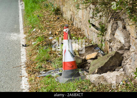 Übrig gebliebene Zerschlagen von fahrzeugtruemmern Ablagerungen einen kunststoffkegel und Band auf einer ländlichen Lane, nachdem ein Auto Kollision mit einer Steinmauer in Großbritannien links Stockfoto