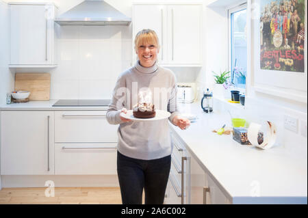 Eine Mutter steht in der Küche mit einem Geburtstagskuchen Und die Kerzen leuchteten Stockfoto