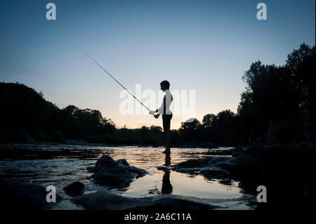 Ein Kind beginnt und am Wasser bei Sonnenuntergang Angeln mit der Rute. Stockfoto