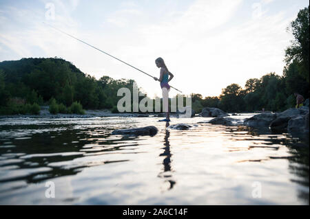 Ein Kind beginnt und am Wasser bei Sonnenuntergang Angeln mit der Rute. Stockfoto