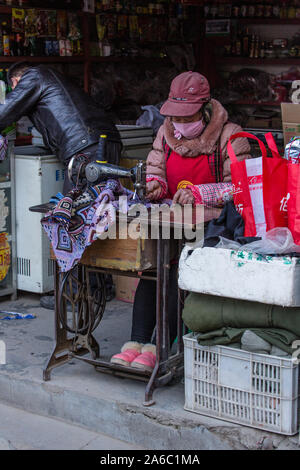 Einer tibetischen Schneiderin näht mit einem Fuß - tritt Nähmaschine vor Ihr Shop in einer Nachbarschaft, in Lhasa, Tibet. Stockfoto