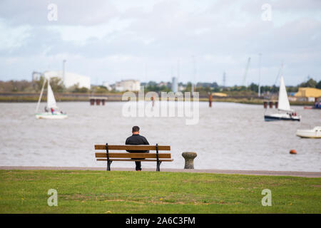 Ein Mann sitzt alleine auf einer Bank neben der Themse in Gravesend, Kent, Großbritannien Stockfoto