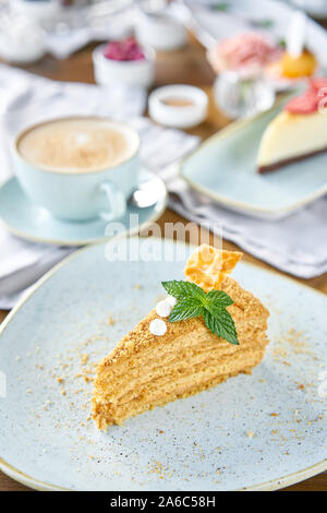 Honig Kuchen mit Baiser und Minze dekoriert.. Frühstück im Café, Kaffee am Morgen. Cappuccino und viele Desserts auf dem Tisch. Stockfoto