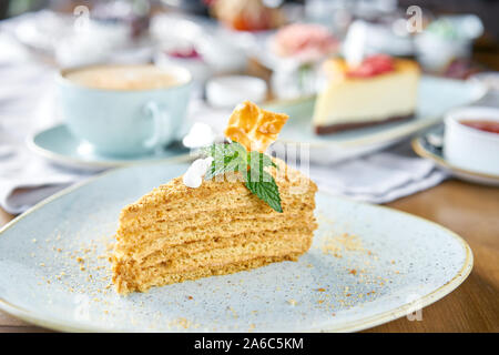 Honig Kuchen mit Baiser und Minze dekoriert.. Frühstück im Café, Kaffee am Morgen. Cappuccino und viele Desserts auf dem Tisch. Stockfoto