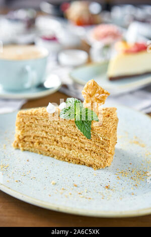 Honig Kuchen mit Baiser und Minze dekoriert.. Frühstück im Café, Kaffee am Morgen. Cappuccino und viele Desserts auf dem Tisch. Stockfoto