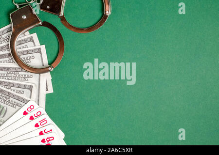 Handschellen liegen neben Karten und US-Dollar auf einem grünen Hintergrund. Glücksspiel Kriminalität Konzept. Copyspace. Stockfoto