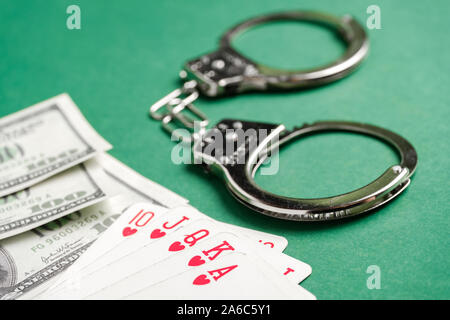Handschellen liegen neben Karten und US-Dollar auf einem grünen Hintergrund. Glücksspiel Kriminalität Konzept. Close Up. Stockfoto