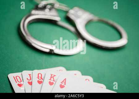 Handschellen liegen neben Karten auf einem grünen Hintergrund. Glücksspiel Kriminalität Konzept. Close Up. Stockfoto