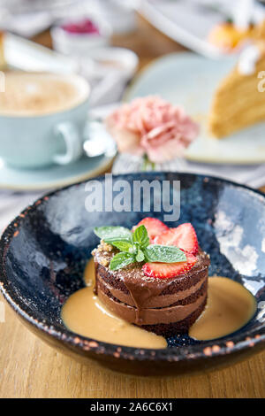 Schokolade Biskuit, mit Karamell, mit Erdbeeren und minzeblatt eingerichtet. Frühstück im Café, Kaffee am Morgen. Cappuccino und viele Desserts Stockfoto