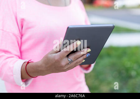 Nahaufnahme des Touchscreen tablet werden durch Frau in rosa Bluse im Sommer auf der Straße verwendet. Ansicht von hinten. Stockfoto