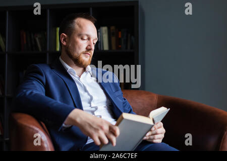 Nach erfolgreicher Geschäftsmann im Anzug sitzt ein Buch zu lesen. Stockfoto