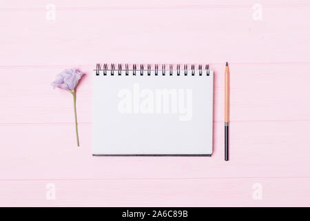Leer Notebook mit Bleistift in der Nähe von Lilac Blume des lisianthus auf rosa Holztisch, flach. Stockfoto