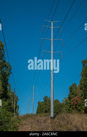 Großes und hohes power line Türme schneiden durch die Wälder mit einer zweiten Linie parallel auf einem hellen Blau sonnigen Himmel im Herbst Stockfoto