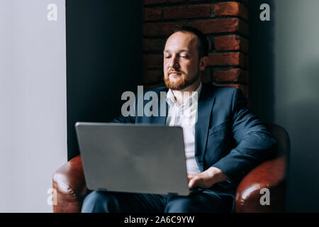 Der bärtige Mann Geschäftsmann sitzt und arbeitet in einem Laptop in einem modernen Interieur. Stockfoto
