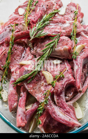 Roh marinierte Lammkoteletts mit Rosmarin, Olivenöl und Knoblauch in Glasschale. Bereit zu kochen und zu essen. Stockfoto