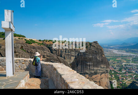 Meteora, Griechenland - 26. Juli 2019; Touristen fotografieren der Felsformationen und Landschaft unter von Lookout mit großen weißen religiösen Kreuz. Stockfoto