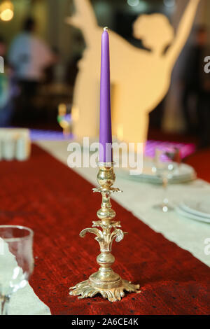 Pastell lila Kerze in Messing antik Kandelaber oder Kerzenständer auf unscharfen Hintergrund mit Kopie Raum. brennende Kerzen auf dem Tisch im Restaurant Stockfoto