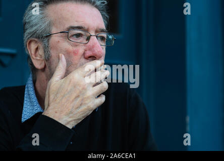 Mittleres alter Mann mit grauen Haaren ist draußen rauchen einer Zigarette allein in der Kneipe sitzen Stockfoto