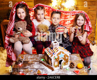 Eine Gruppe kleiner Kinder spielen mit Spielzeug auf dem Hintergrund von Weihnachten Dekor und Lebkuchenhaus. Stockfoto