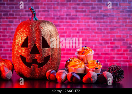 Halloween Kürbis mit halloween Muffins und Ornamente mit roter Beleuchtung Stockfoto