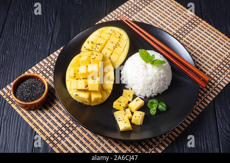Klebreis mit Mango bestreut mit Sesam auf einer schwarzen Platte auf einem Holztisch, thailändische Küche, horizontale Ansicht von oben, close-up Stockfoto