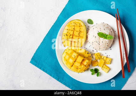 Cremige klebrigen Reis mit Kokosmilch gekocht und serviert mit frischen Mango auf einer weißen Platte mit Stäbchen, horizontale Ansicht von oben, flach Stockfoto