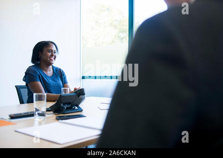 Eine schwarze Frau sitzt an einem Tisch in einer Chancengleichheit Business Stockfoto