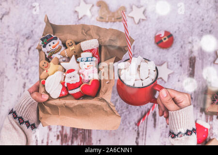 Frau Hände halten ein Weihnachten Lebkuchen Plätzchen in einer Box und heiße Schokolade mit Marshmallows. Weihnachtsgeschenke, Kakao trinken in rot Tasse und New Y Stockfoto