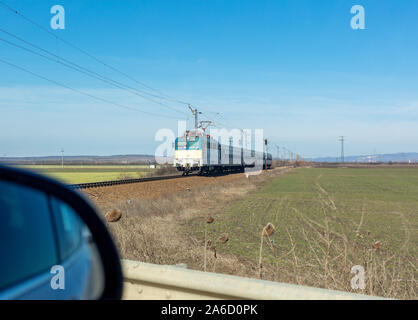 Blick auf den herannahenden Zug und ein Teil der Außenspiegel des Autos vor Bahnübergang Stockfoto