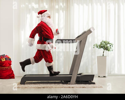 Volle Länge Profil Schuß von Santa Claus auf einem Laufband zu Hause Stockfoto