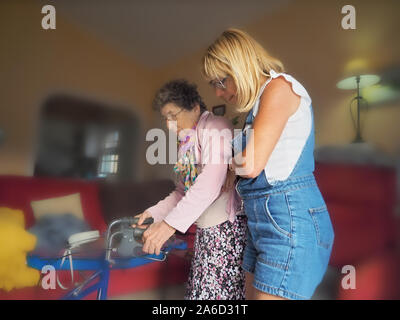 Eine Altenpflegerin führt eine sehr alte und behinderte Senior mit ihr zu Fuß wagen, r. Selektive konzentrieren. Stockfoto