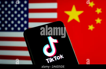 TikTok app Logo auf einem Bildschirm des Smartphones und Fahnen von China und USA auf die verschwommenen Hintergrund. Die App ist in der Mitte der Spannungen zwischen den USA und China. Stockfoto